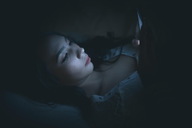 Aziatische vrouw speelspel op smartphone in het bed 's nachts Thailand peopleAddict social media