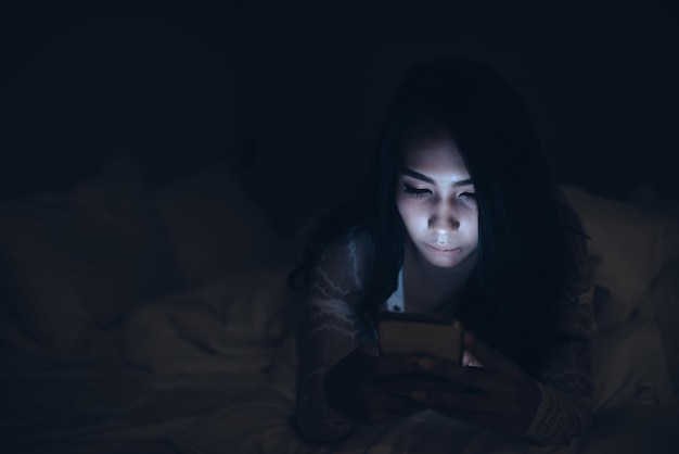 Aziatische vrouw speelspel op smartphone in het bed 's nachts Thailand peopleAddict social media
