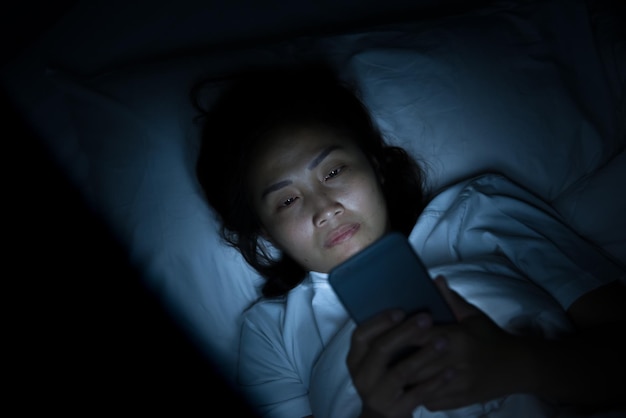 Aziatische vrouw speelt smartphone 's nachts in bed Thailand mensen