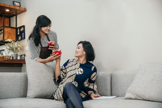 Aziatische vrouw twee die wanneer het zitten in de woonkamer babbelt