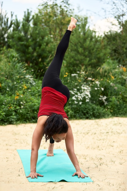 Aziatische vrouw van middelbare leeftijd die yoga doet in het park op het zand tussen de bomen, het concept van yoga, meditatie, ontspanning.