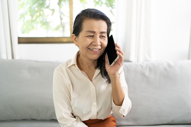 Aziatische vrouw van middelbare leeftijd met een mobiele telefoon, glimlachend, mooie, volwassen Aziatische vrouwen die met een smartphone praten met een technologisch concept.