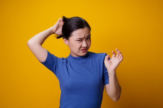 Aziatische vrouw verveeld en geïrriteerd, haar hoofd krabben, op geel.