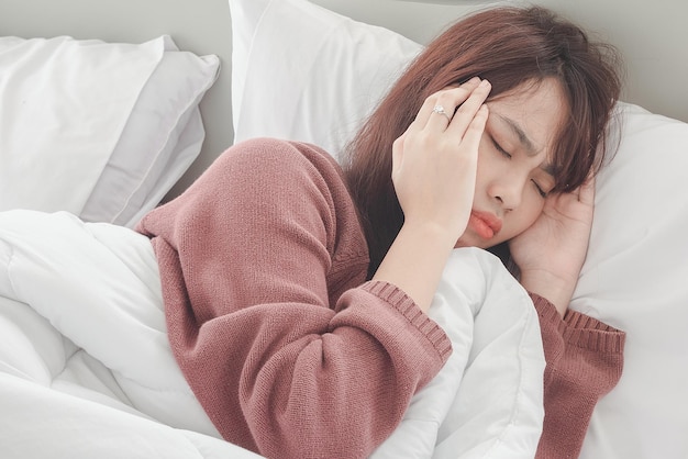 Aziatische vrouw voelt hoofdpijn en ongemak op bed in de ochtend van de witte slaapkamer