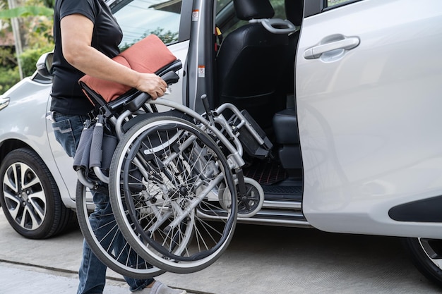 Aziatische vrouw vouwt en tilt rolstoel op in haar auto Toegankelijkheidsconcept