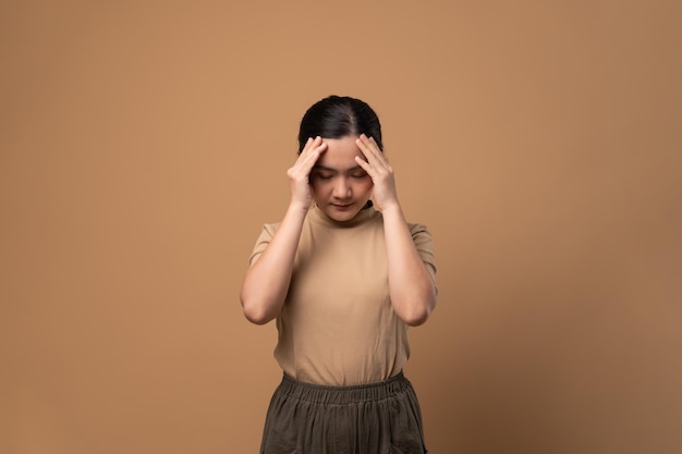 Aziatische vrouw was ziek van hoofdpijn die haar hoofd aanraakte en geïsoleerd stond op een beige achtergrond