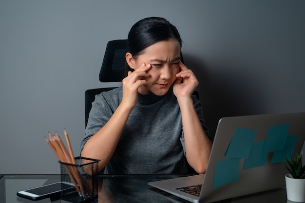 Aziatische vrouw was ziek van oogpijn, raakte haar ogen aan, werkte op een laptop op kantoor