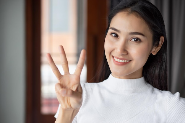 Aziatische vrouw wijzend tellen drie vingers portret van gelukkig lachende Aziatische vrouw die 3 vingers omhoog wijst voor nummer drie of 3 punten concept door Chinese Aziatische volwassen vrouw model casual thema binnen