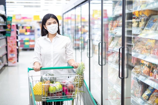 Aziatische vrouw winkelen met masker veilig kopen voor boodschappen, veiligheidsmaatregelen in de supermarkt.