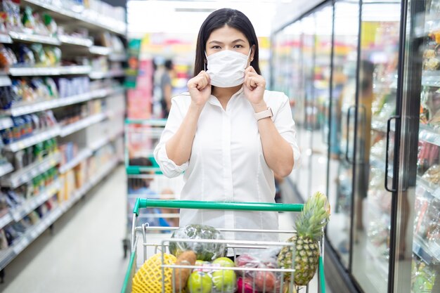 Aziatische vrouw winkelen met masker veilig kopen voor boodschappen, veiligheidsmaatregelen in de supermarkt.