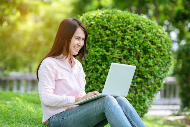 Aziatische vrouw zit groen park met behulp van laptopcomputer Vrouw werkt aan laptop gelukkig ondernemersbedrijf met behulp van notebook met handen typen op toetsenbord thuiskantoor tijdens coronavirus quarantaineperiode