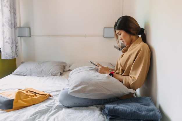 Aziatische vrouw zit op het bed in een kleine slaapkamer van een goedkoop hotel