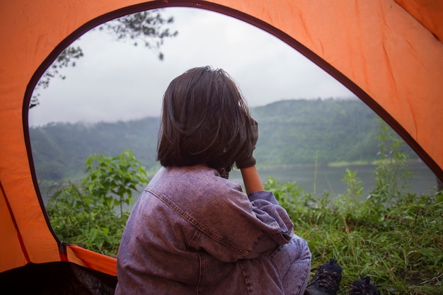 Aziatische vrouw zitten in tent en kijken naar het uitzicht op het meer van de bergen in zonsondergang tijd op camping vakantie vakantie