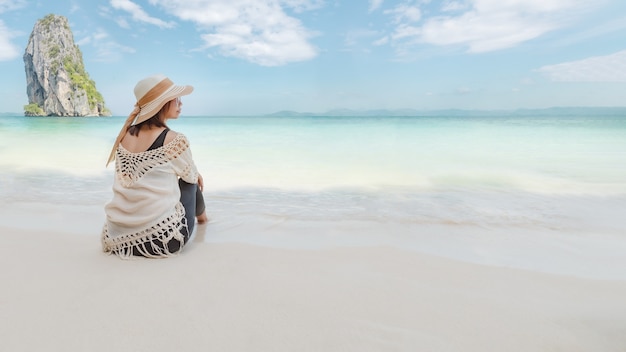 Aziatische vrouw zittend op het strand kijken naar de geweldige zee en genieten met prachtige natuur in haar vakantie. Zomervakantie concept.