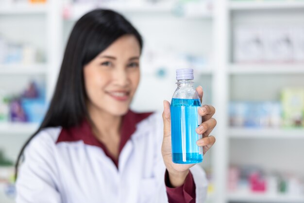 Aziatische vrouwelijke apotheker toont fles handgel in drogisterij Thailand close-up en selectieve aandacht blauwe gel op handapotheker