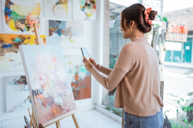 Aziatische vrouwelijke artiest die foto's maakt van haar eigen schilderij met smartphone