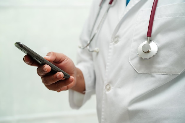 Aziatische vrouwelijke arts met een mobiele telefoon of tablet voor het zoeken naar een behandelingsmethode voor een patiënt in het ziekenhuis