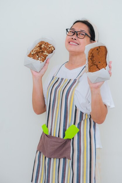 Aziatische vrouwelijke bakker die een schort draagt en haar twee broden fruitcake in beide handen laat zien