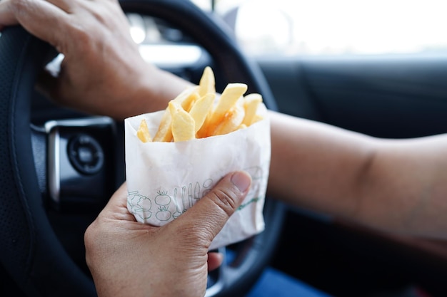 Aziatische vrouwelijke bestuurder houdt en eet frietjes in de auto gevaarlijk en riskeert een ongeval