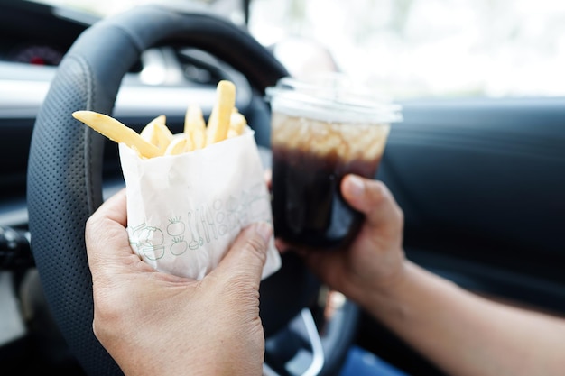 Aziatische vrouwelijke bestuurder houdt en eet frietjes in de auto gevaarlijk en riskeert een ongeval