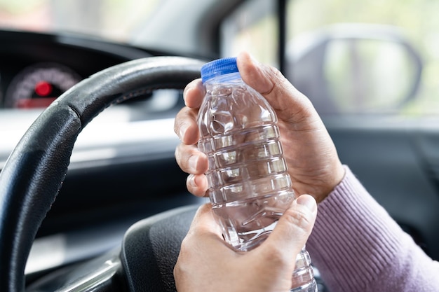 Aziatische vrouwelijke chauffeur die een fles vasthoudt om water te drinken tijdens het autorijden Plastic warmwaterkruik veroorzaakt brand