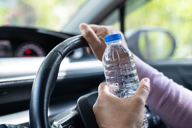 Aziatische vrouwelijke chauffeur die een fles vasthoudt om water te drinken tijdens het autorijden Plastic warmwaterkruik veroorzaakt brand