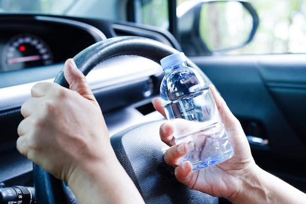 Aziatische vrouwelijke chauffeur houdt koud water vast voor drank in de auto, gevaarlijk en riskeert een ongeluk