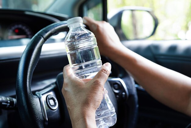 Aziatische vrouwelijke chauffeur houdt koud water vast voor drank in de auto, gevaarlijk en riskeert een ongeluk