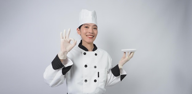 Aziatische vrouwelijke chef-kok met smartphone of digitale tablet en bestelling ontvangen van online winkel of handelsapplicatie. ze lacht in uniform van de chef-kok en staat op een witte achtergrond. Online handelaar in levensmiddelen.
