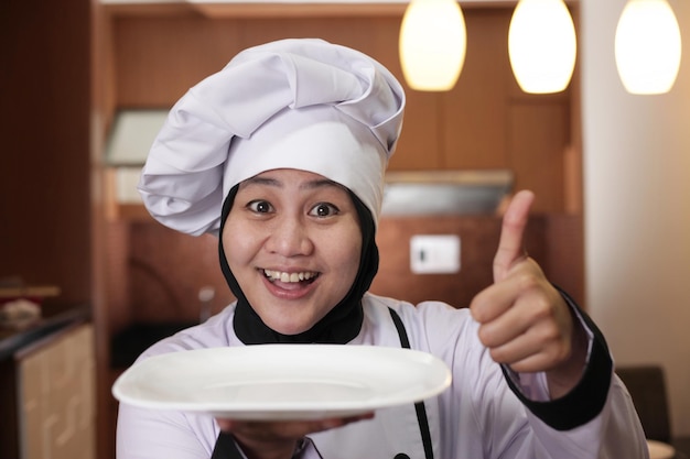 Foto aziatische vrouwelijke chef-kok toont leeg wit bord dat iets presenteert