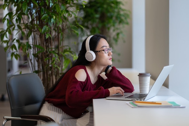 Aziatische vrouwelijke freelancer in hoofdtelefoons werkend laptopscherm in coworking space of openbare bibliotheek