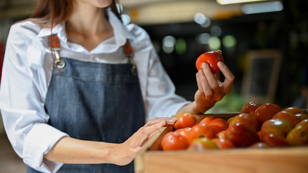Aziatische vrouwelijke kleine lokale supermarkteigenaar die haar biologische tomaten schikt