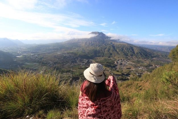 Aziatische vrouwelijke reiziger die achter de Batur-berg staat vanuit het dorp Pinggan, gelegen in Kintamani Bangli Bali, Indonesië