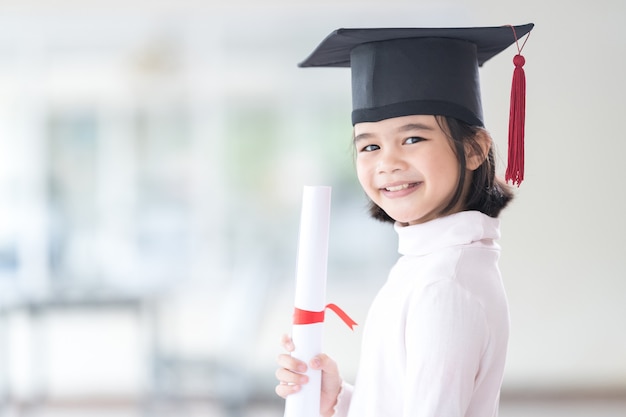 Foto aziatische vrouwelijke schooljongen afgestudeerd in een afstudeerpet heeft een opgerold certificaatpapier