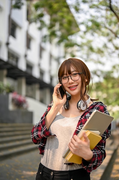 Aziatische vrouwelijke student die aan de telefoon praat terwijl ze buiten het campusgebouw staat