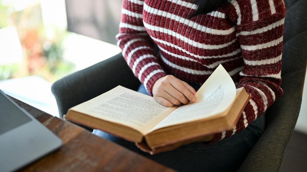 Aziatische vrouwelijke student die een boek leest terwijl ze in de campusbibliotheek zit bijgesneden afbeelding