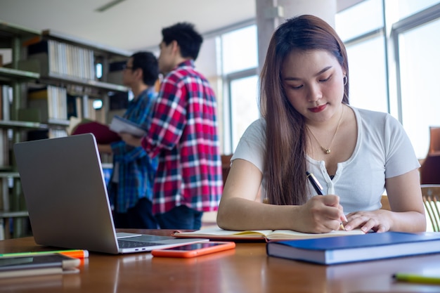 Aziatische vrouwelijke student zit en doet haar huiswerk in de bibliotheek