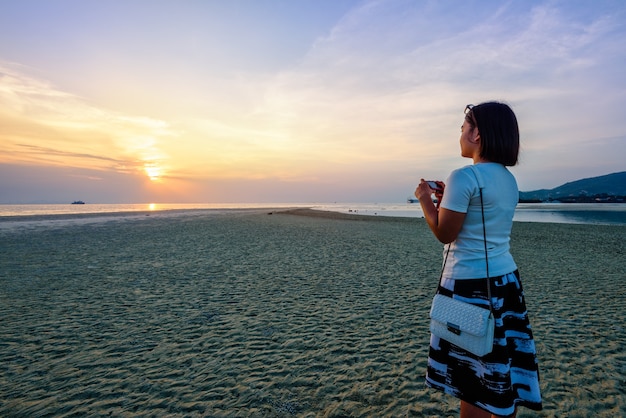 Aziatische vrouwelijke toerist die foto neemt op het strand en het prachtige natuurlijke landschap van kleurrijke lucht en zee tijdens een zonsondergang bij Nathon Sunset Viewpoint op het eiland Samui, Surat Thani, Thailand