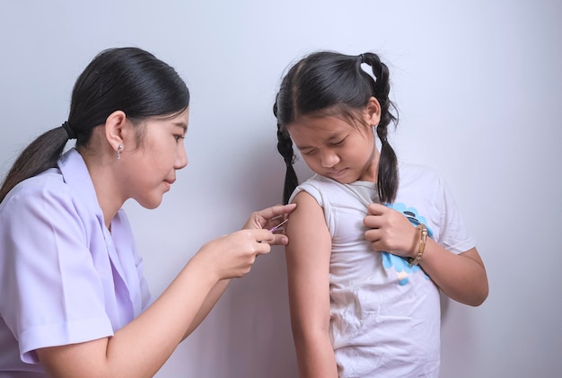 Aziatische vrouwelijke verpleegster die vaccin geeft aan meisje in kliniek