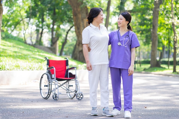 Aziatische vrouwelijke verpleegster die voor een vrouwelijke patiënt van middelbare leeftijd in het park zorgt