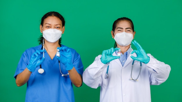 Aziatische vrouwelijke verpleegster in scrubs en arts in witte jurk met masker met spuit en covid 19-vaccin dat zich voorbereidt op injectie. concept voor covid 19-vaccinatie.