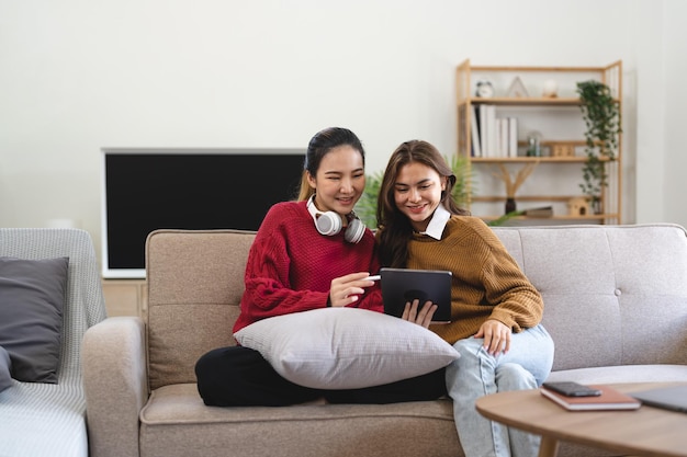 Aziatische vrouwelijke vrienden zitten in de woonkamer en kijken samen naar film op tablet Moderne vrouwelijke vriendschap geniet thuis van een weekendactiviteitslevensstijl met draadloze technologie