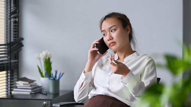 Aziatische vrouwelijke werknemer die een mobiel telefoongesprek voert in een modern kantoor