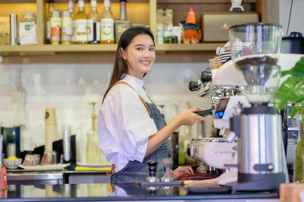 Aziatische vrouwen Barista glimlachend en met behulp van koffiemachine in de balie van de coffeeshop