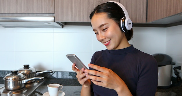 Aziatische vrouwen die hoofdtelefoon dragen en aan muziek in de keuken thuis luisteren