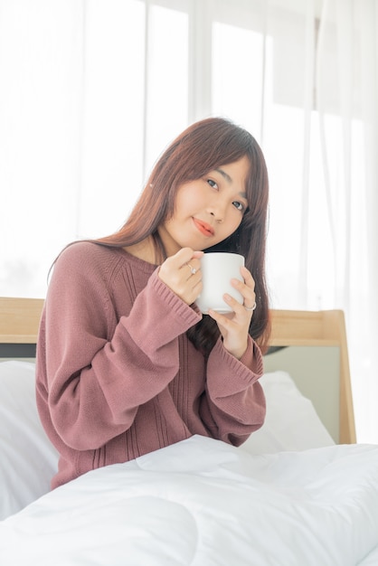 Aziatische vrouwen die koffie op bed in de ochtend drinken