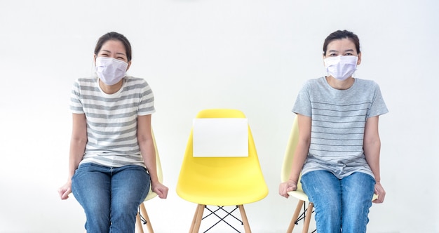 Aziatische vrouwen die maskers dragen, zitten op de stoel met papier of kopiëren ruimte voor tekst, maken sociale afstand en maken een nieuwe normale levensstijl tijdens de uitbraak van Covid-19.