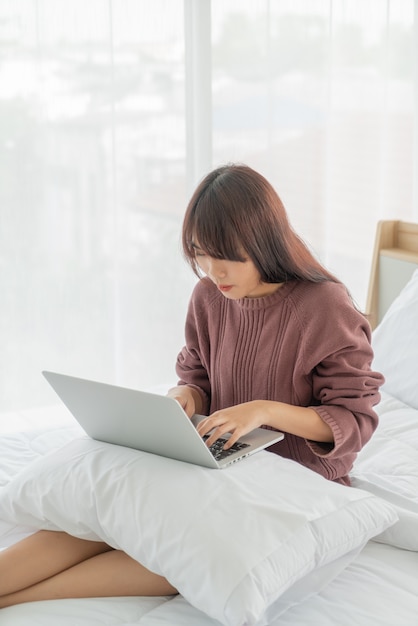 Aziatische vrouwen die met laptop aan bed werken