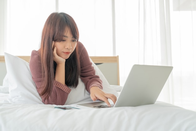 Aziatische vrouwen die met laptop op bed thuis werken