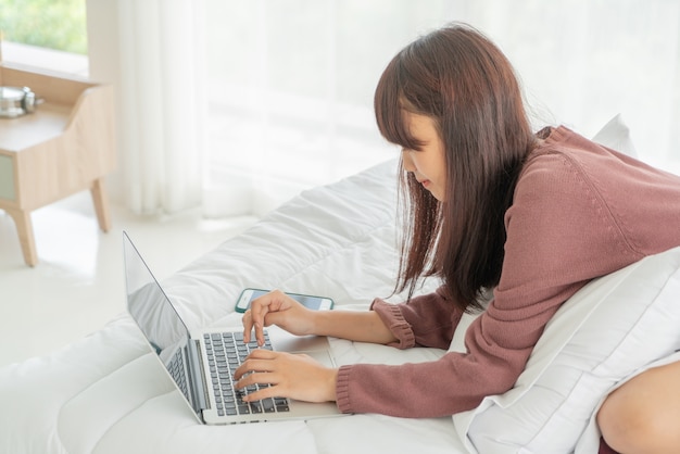 Aziatische vrouwen die met laptop op bed thuis werken